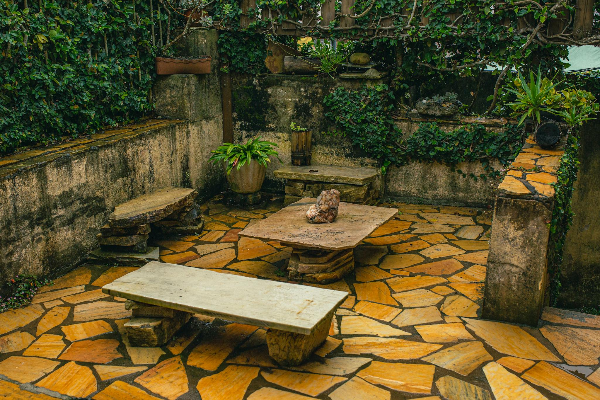 A cozy stone garden patio with ivy-covered walls, stone benches, and rustic decor perfect for relaxation.